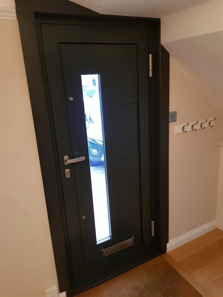 Dark anthracite composite front door seen from inside a hallway, with daylight through its tall glazed panel