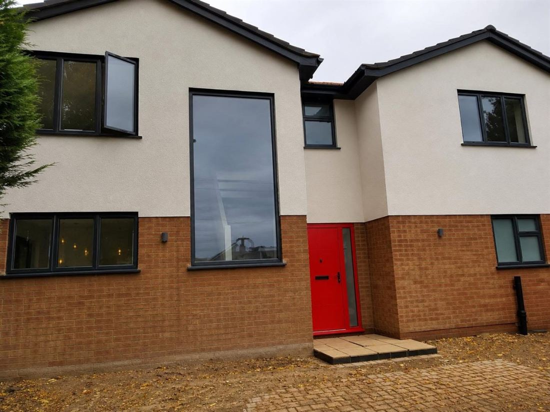 Front elevation of a new-build house with anthracite grey aluminium windows, a full-height fixed pane and a red composite front door with sidelight