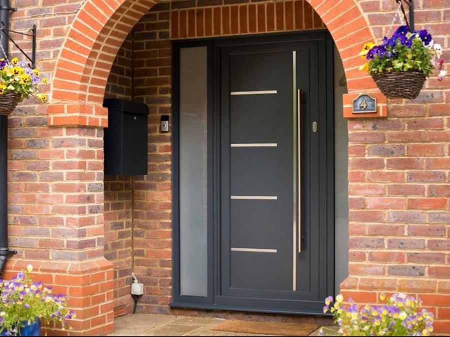 Anthracite grey composite front door with a long brushed steel bar handle and obscure glazed sidelight, set in an arched brick porch